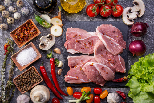 Raw pork steaks, fresh vegetables, spices close-up on a textured background