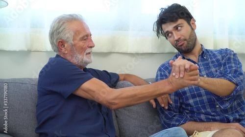  Happy family senior father talking and having fun with son on sofa in living room. Smiling old age dad spending time together with adult man son at home. Family bonding and good relationship concept