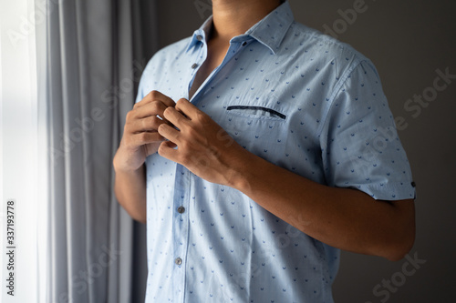Men button blue shirts on weekdays in a room standing near the window