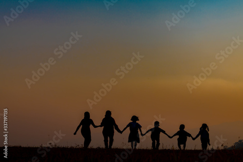 The silhouette of the team of children jumping playing with joy in the mountains in the setting sun
