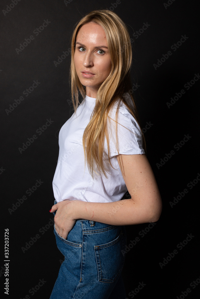 Beautiful young woman poses looking at camera. Hands in pocket. Black backgroung Beautiful young woman poses looking at camera. Hands in pocket. Black backgroung