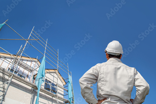 建設中の戸建て住宅を見る作業着姿の男性の後ろ姿。