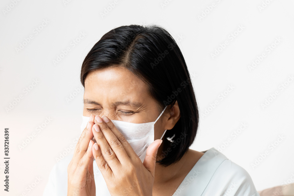 Woman sneezing under face mask covering mouth and nose while coughing. Suspect people have to make 14-day Self-Quarantine. Corona Virus or COVID-19 concept. Woman sneezing under face mask covering mouth and nose while coughing. Suspect people have to make 14-day Self-Quarantine. Corona Virus or COVID-19 concept.