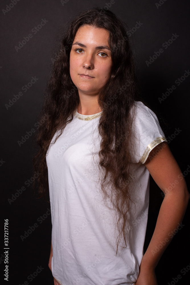 Young caucasian girl looking relaxedly. Hands in pocket. Black background
