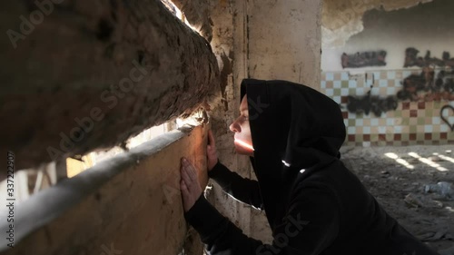 woman looks through gap in boarded up window in abandoned building. photo