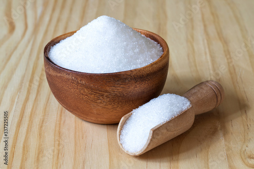 Bowl and scoop with white sand sugar on wooden background..