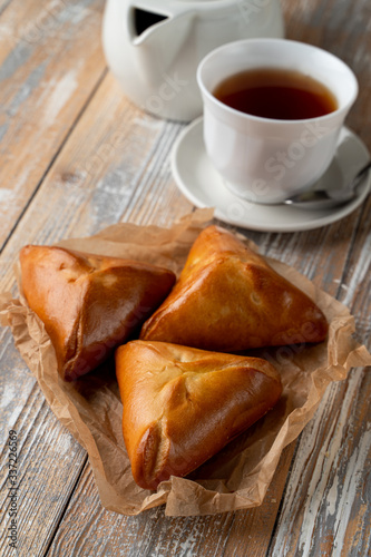 Traditional russian stuffed pierogi bake with golden crust, served on wooden table with a cup of tea
