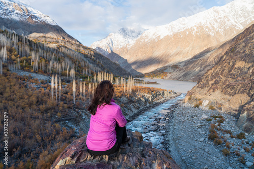 A woman traveller sitting on rock and looking to beautiful mountain landscape in autumn season in Gupis valley, Pakistan photo