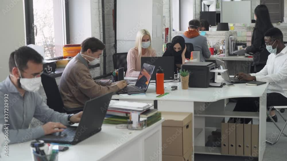 International office, working and communicate in an open space, office workers and managers in medical masks working at computers, protection from the virus, working during the pandemic.