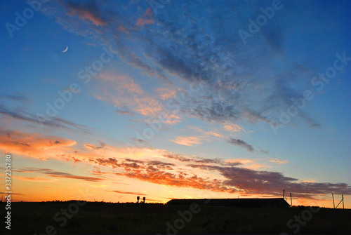 Beautiful sunset with moon over farm silhouette  sunlight on horizon of golden pink sky with clouds