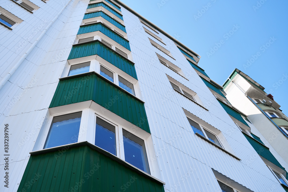 facade of a new multi-storey building with white and green metal siding, many Windows