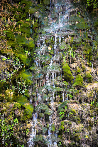 The beautiful waterfall descends through the mountains with the background of plants and trees.