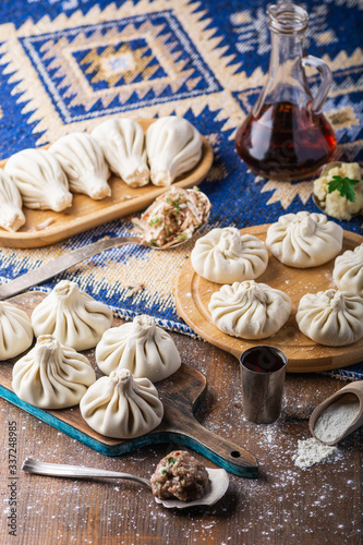 Traditional Caucasian cuisine. Raw dumpling or khinkali with meat, mushroom and potato laid out on a cutting board on a wooden table with a towel, rolling pin, vegetables and spices.