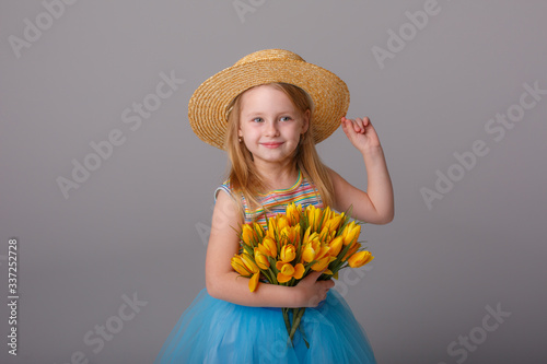 a little girl in a straw hat holding a yellow flower