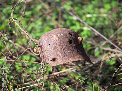 Wehrmacht Rusty M35 Helmet WWII Damaged By Bullets And Shrapnel. Metal Helmet Of German Infantry Wehrmacht Soldier At World War II. Rusty Helmet Hanging On Tree Trunk. photo