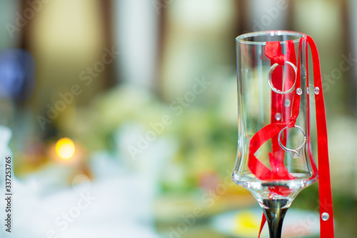 The rings hung from a red ribbon. Wedding bouquet in the background . rings and ribbons are placed inside the glass . Two wedding rings hung from a tree branch .