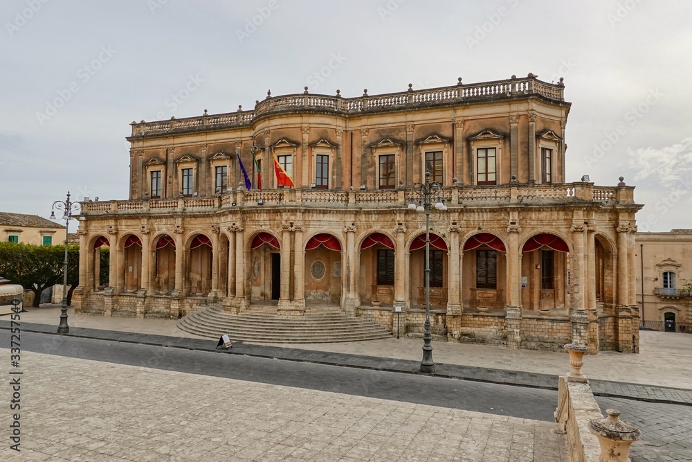 The Palazzo Ducezio in Noto, Sicily, Italy with a rounded staircase in front of the entrance and no people The Palazzo Ducezio in Noto, Sicily, Italy with a rounded staircase in front of the entrance and no people