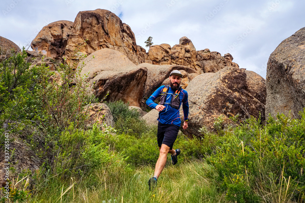 Male runner running on a mountain trail. Athlete runs in the mountains among the rocks. Man in blue jersey and black shorts training outdoors