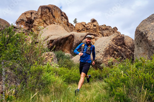 Male runner running on a mountain trail. Athlete runs in the mountains among the rocks. Man in blue jersey and black shorts training outdoors