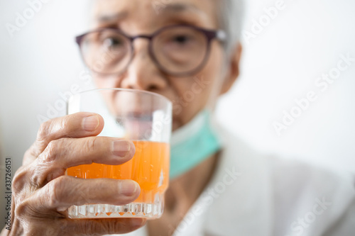 Healthy asian senior woman is drinking a glass of vitamin C or orange juice,elderly people with effervescent vitamin C,strengthening the immunity for cold,flu,fight the Coronavirus,against of Covid-19 photo