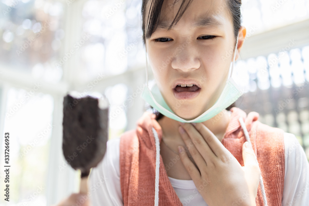 Sick asian child girl with a flu,dry cough and a sore throat,eating too  much ice cream,loss of taste and sense of tasting food or illness from  Coronavirus,Covid-19 infection symptoms,health problems Stock Photo