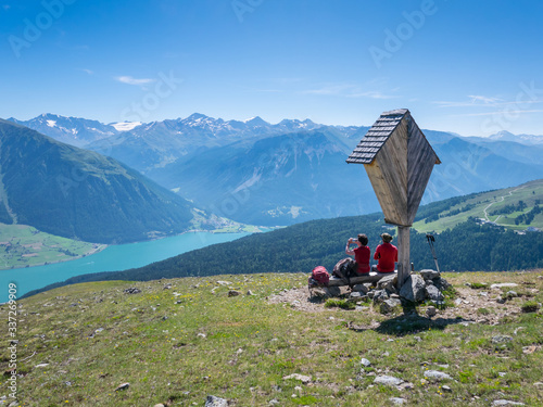 Couple of two medium age hikers resting near a wayside cross above lake Reschen/Resia, Tyrol, Italy photo