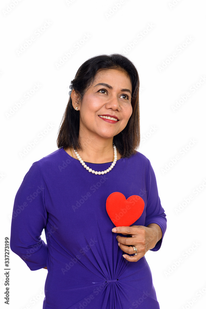 Studio shot of happy mature Asian woman holding red heart isolated against white background Studio shot of happy mature Asian woman holding red heart isolated against white background