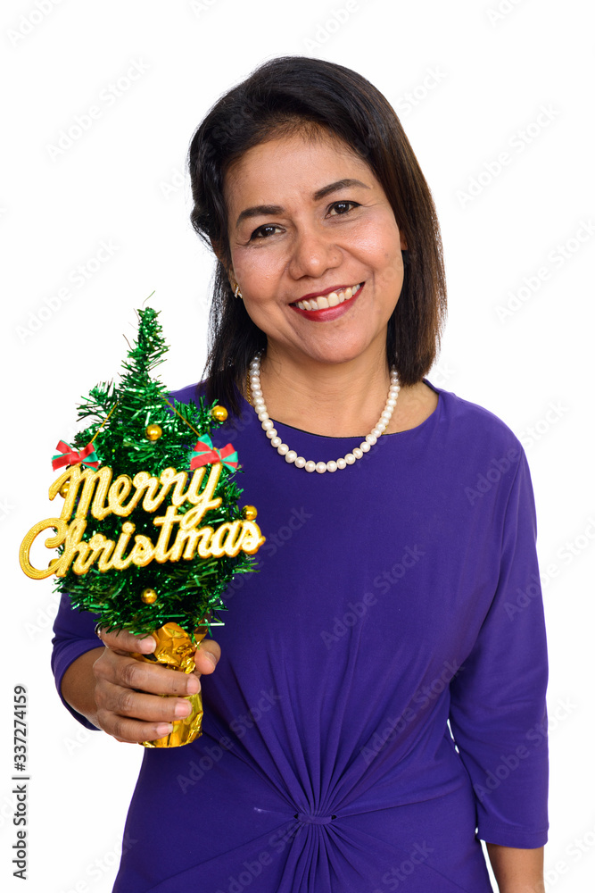 Studio shot of happy mature Asian woman holding Merry Christmas tree isolated against white background Studio shot of happy mature Asian woman holding Merry Christmas tree isolated against white background