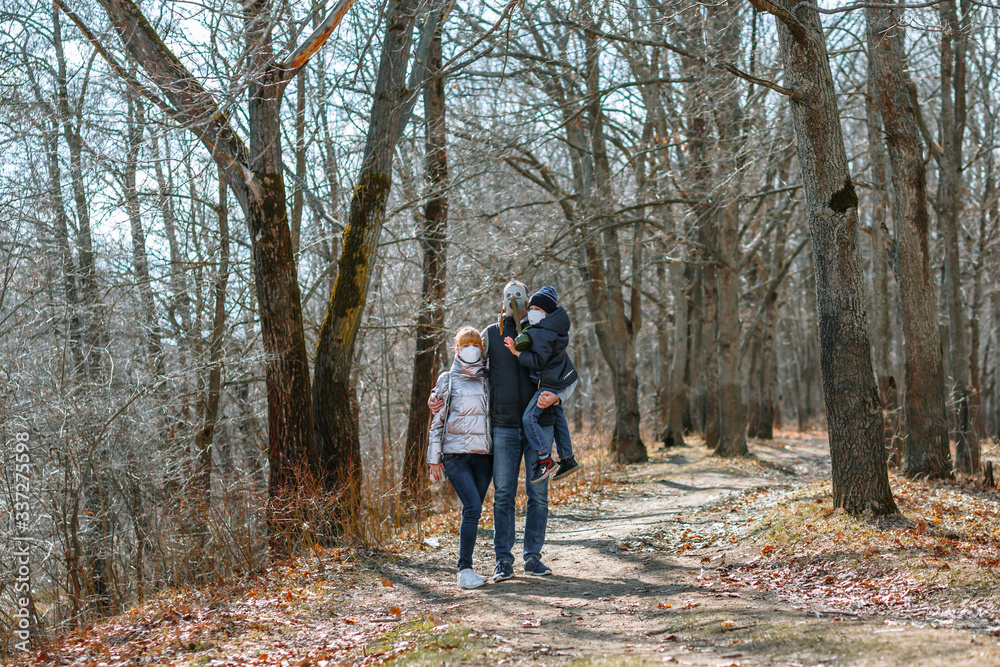 A small family in sanitary masks on a walk in the Park. People walk in the conditions of the quarantine A small family in sanitary masks on a walk in the Park. People walk in the conditions of the quarantine