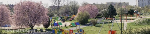 wiosenna panorama z placem zabawa dla dzieci, kwitnące drzewa i krzewy, przyrządy do zabaw i ćwiczeń, pusty plac w okresie pandemii