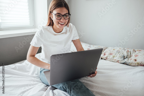 Young smiling woman uses laptop at home on the bed. Communication, video call, remote business