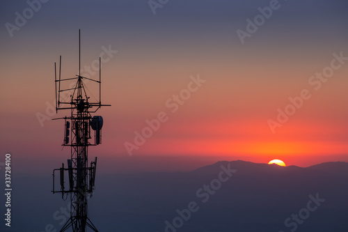 Antena de telecomunicaciones a contraluz con paisaje de montañas en el fondo al anochecer