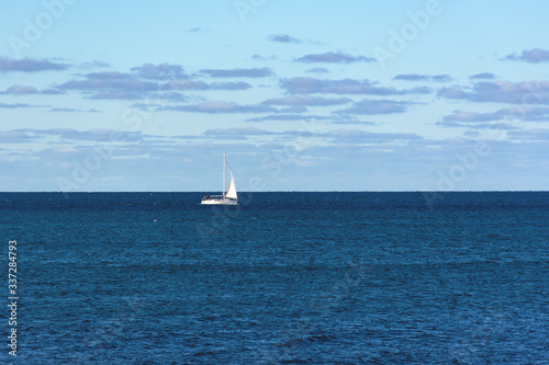 A sailboat cruises on boundless seas. A white sailboat on a blue sea. Classic blue color of the sea