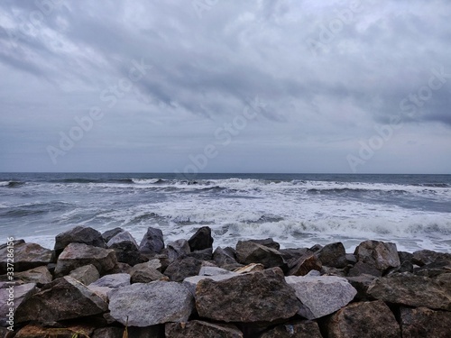 A picture of beach with rocks on the shore and cloudy sky on background. The sea is violent with strong waves in this picture. Kappil Beach (Varkala Town), Kerala.