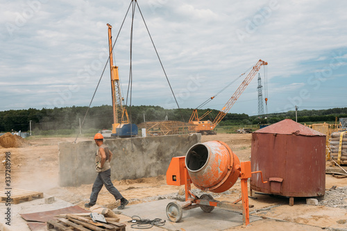 construction worker in an orange helmet next to a concrete mixer at a construction site