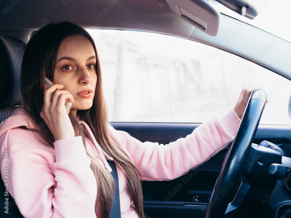 Young girl in pink pite speaks on the phone while sitting in a car.