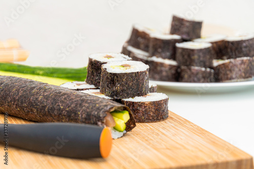 Sushi roll Japanese food rolls ingredients and knife on bamboo kitchen board