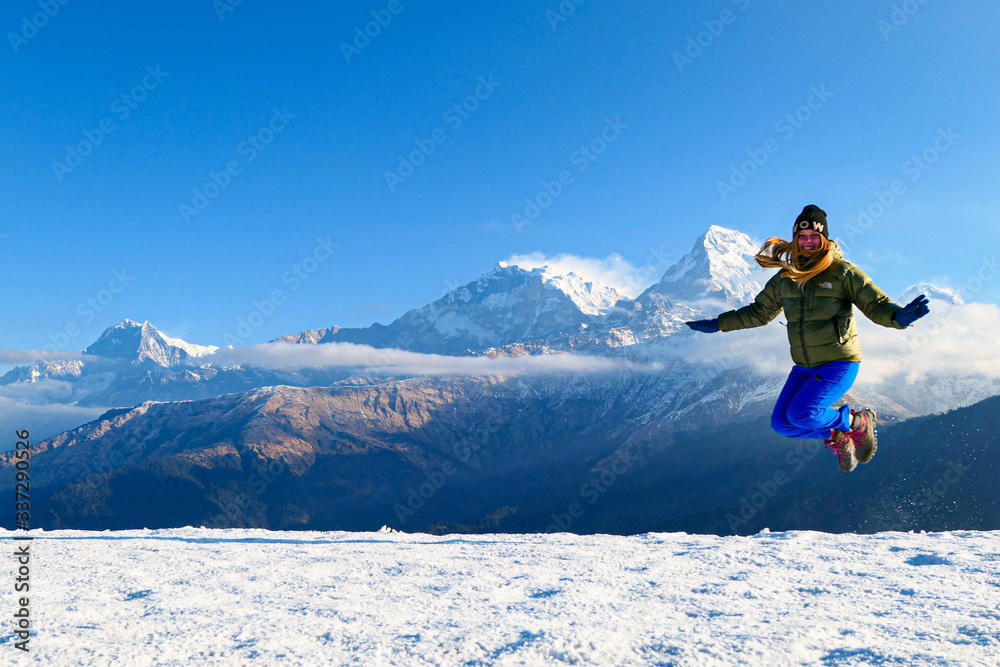 Girl is jumping in front of the mountains. White clouds. Green forest.