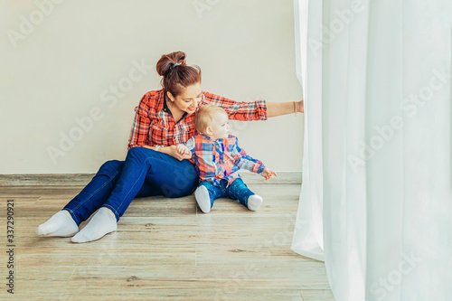 Stay Home Stay Safe. Young mother holding her child. Woman and infant little girl relaxing in white bedroom near windiow indoors. Happy family at home. Young mom playing whith her daughter. photo