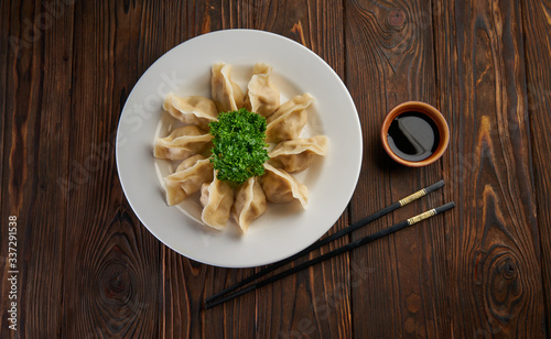 Traditional asian fried dumplings gyoza on white plate and soy sauce with pair of chopsticks on dark wooden background top view and copy space