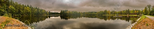 view on a pond from a dyke with forest and dark cloudy sky reflected on water surface