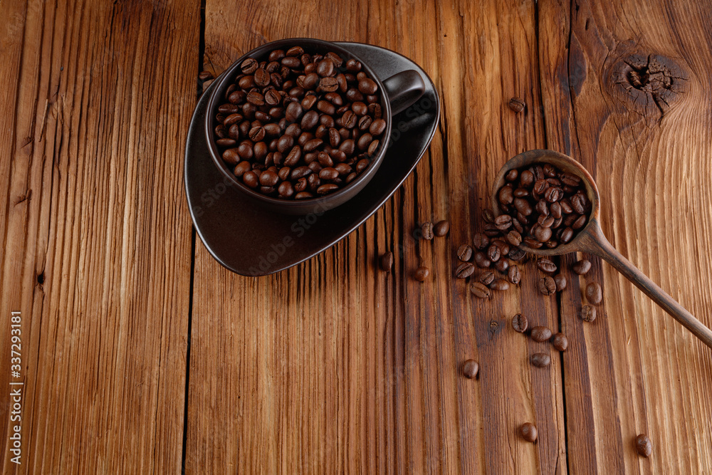 Coffee beans in a wooden spoon and cup with coffee on a wooden table. Selective focus Coffee beans in a wooden spoon and cup with coffee on a wooden table. Selective focus