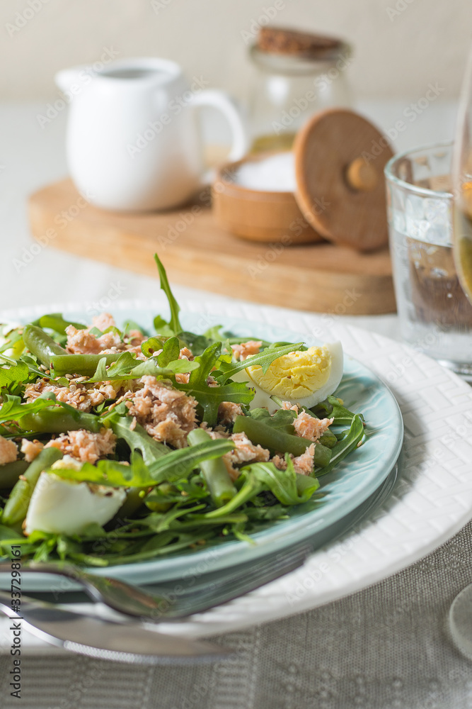 Arugula and trout salad with egg and asparagus on a plate on a table covered with a tablecloth with a glass of wine and a glass of water. Vertical arrangement Arugula and trout salad with egg and asparagus on a plate on a table covered with a tablecloth with a glass of wine and a glass of water. Vertical arrangement