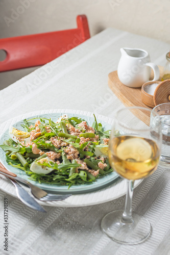 Arugula and trout salad with egg and asparagus on a plate on a table covered with a tablecloth with a glass of wine and a glass of water in the background chair