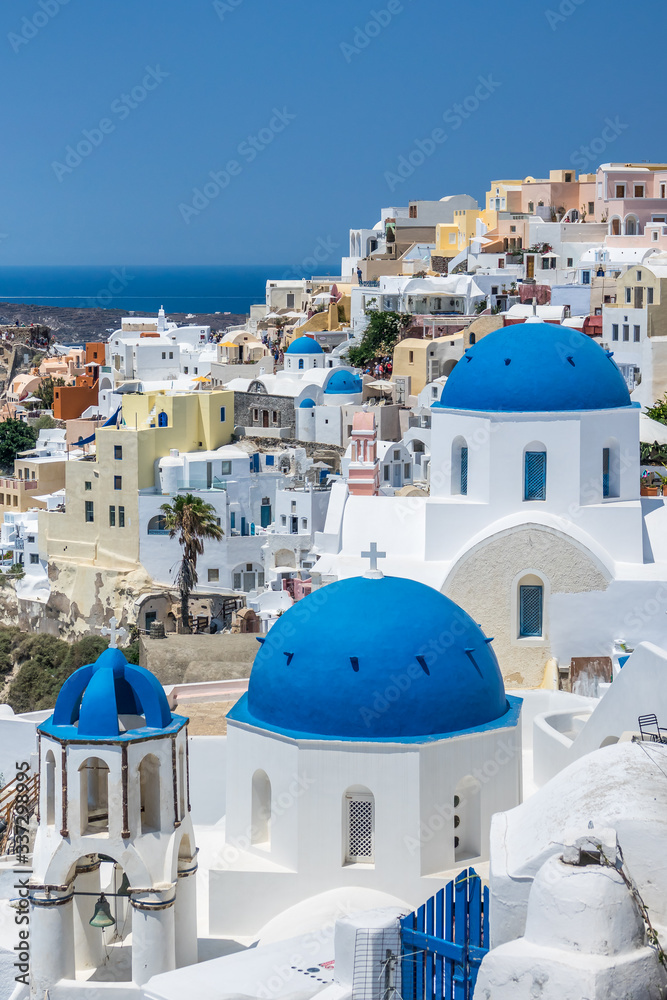 Iconic three blue domes in Oia Santorini against the town of Oia and the sea behind it