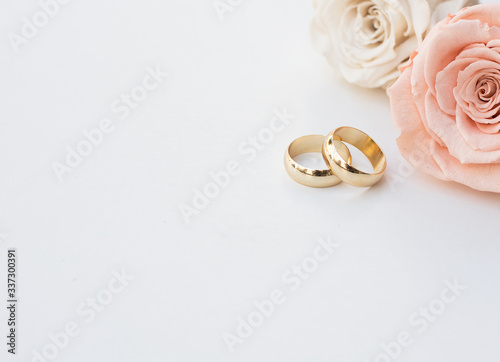 Golden wedding rings and two roses in soft tones on white background photo