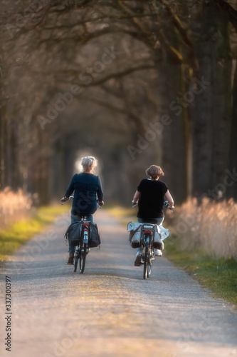 Two mature women cycling on sunny country road in early spring.