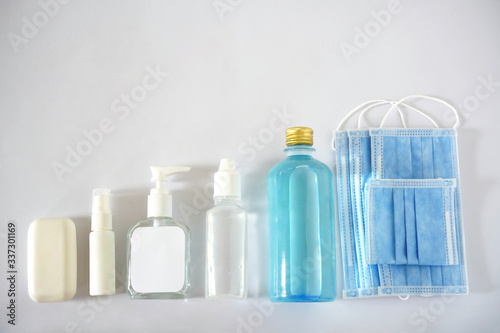 A collection of first aid objects for Corona virus or Covid 19 protection. Four blue face masks, alcohol, saline, pump bottle, spray and soap are on white background. Flat lay.