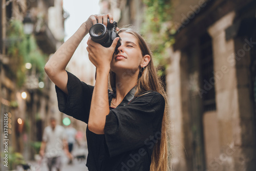 Female tourist photographer is trying to catch the moment, she picked up her photo camera, pressed it to her face and started to take pictures. She is smiling and enjoying the streets of the city