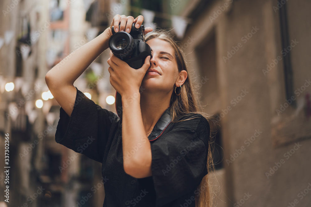 Female tourist photographer is trying to catch the moment, she picked up her photo camera, pressed it to her face and started to take pictures. She is smiling and enjoying the streets of the city